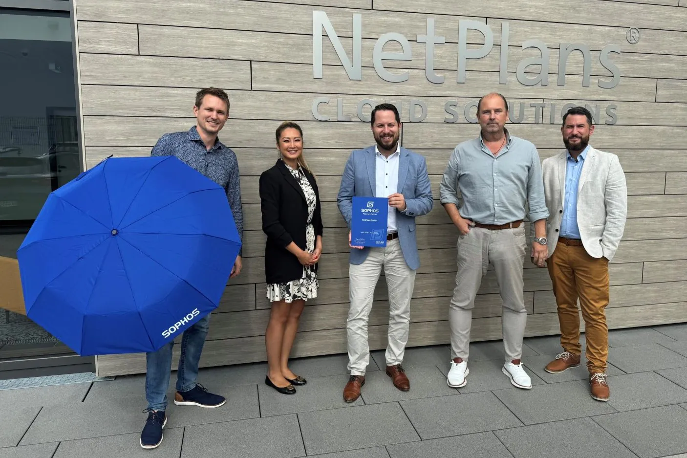 NetPlans Mitarbeiter und SOPHOS Mitarbeiter stehen vor dem NetPlans Logo mit einem SOPHOS Regenschirm